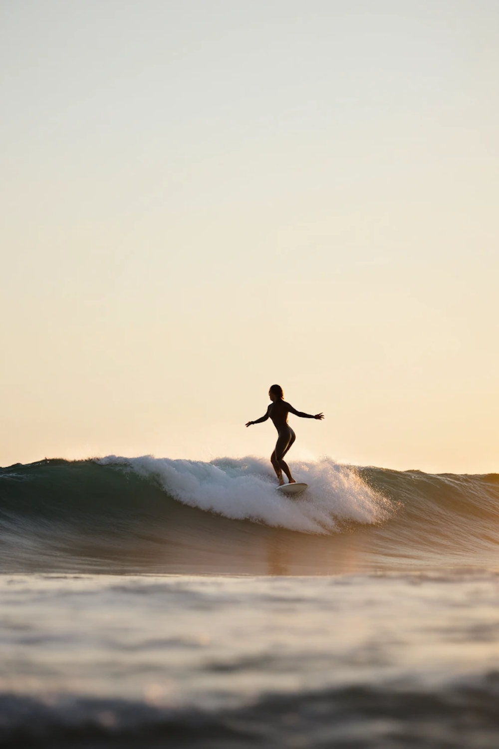 Surfer silhouetted against a golden sunset wave